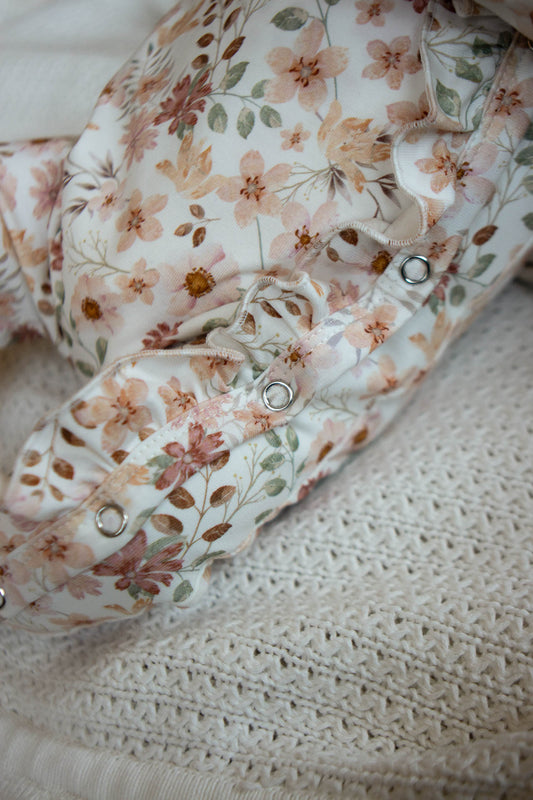 Pfirsichfarbener Strampler mit Rüschen und Blumen